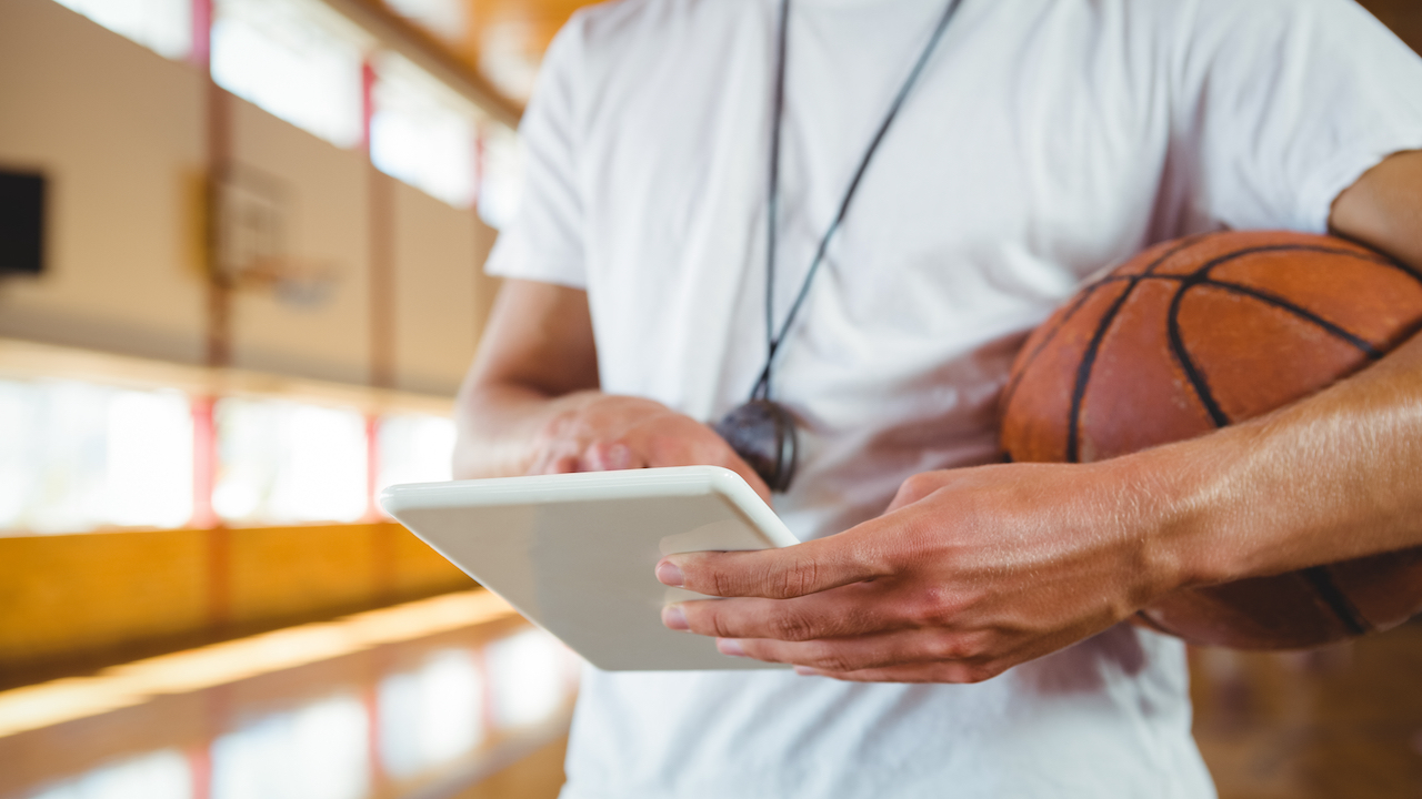 Basketball coach using smart device on basketball court.